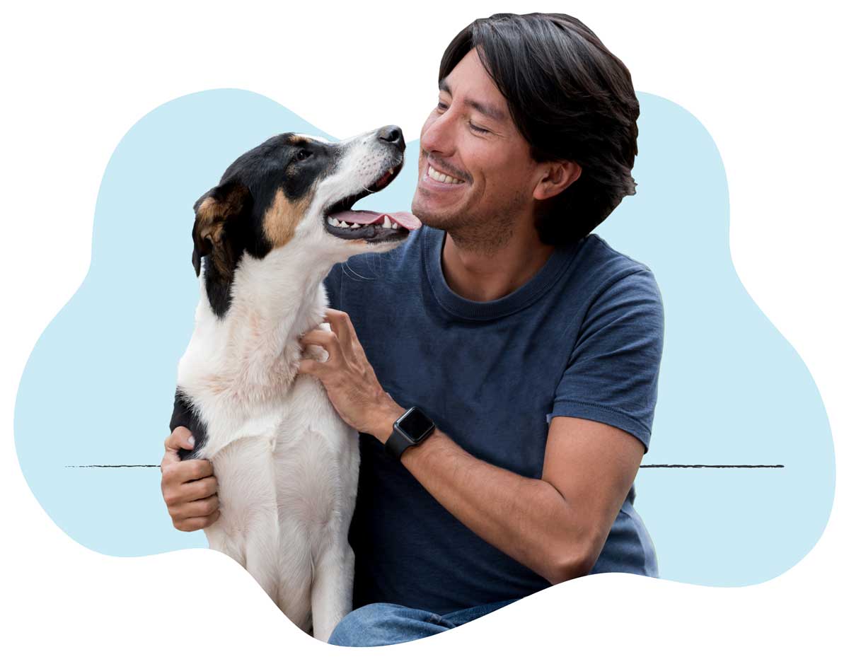 A man sitting next to and smiling at his happy dog