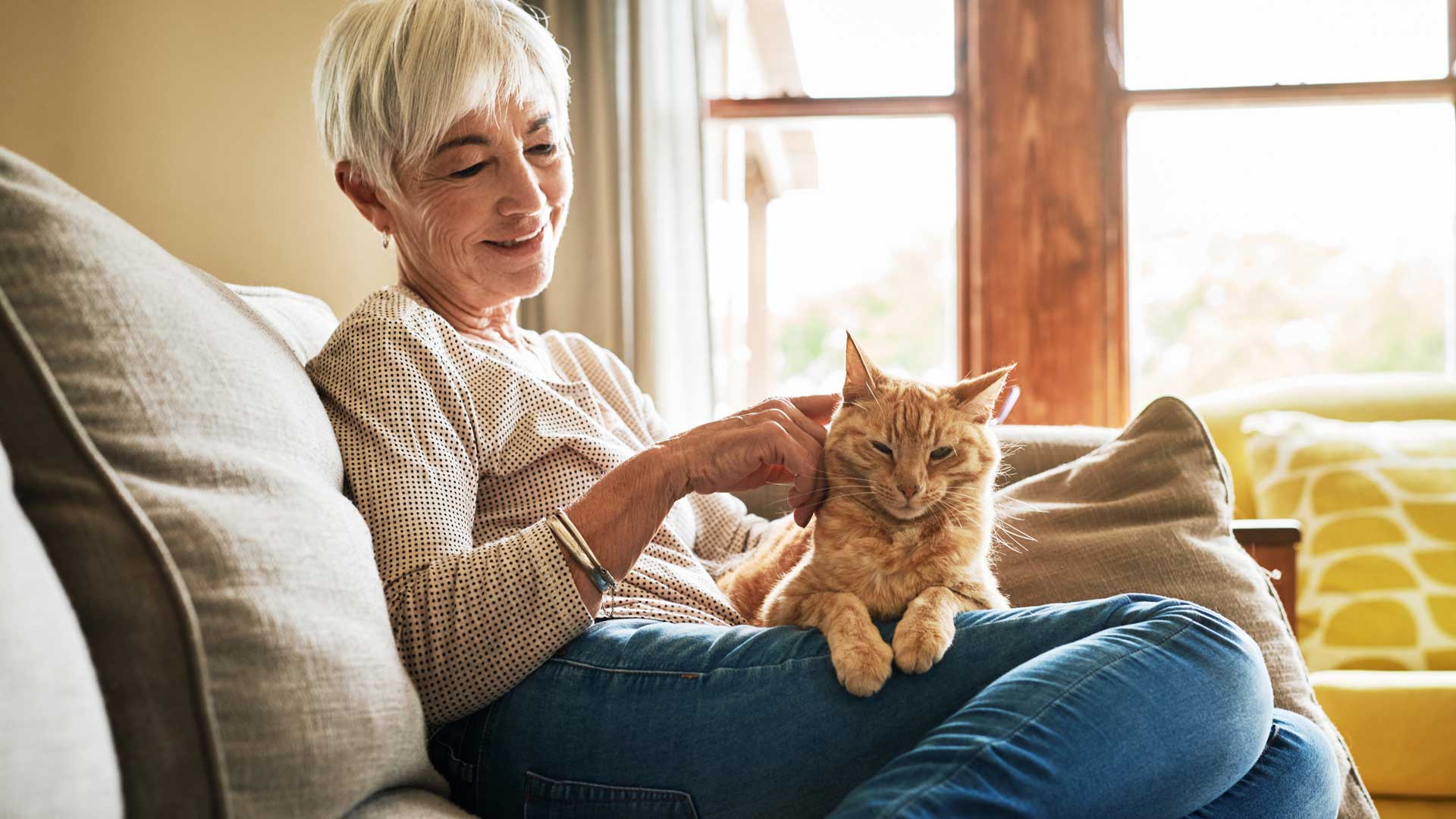 An older woman sits on the couch with her orange cat